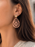 Boucles d'oreilles pendantes en acrylique rose poudré découpé à motif arabesque, avec puce ronde dorée martelée, portées par une femme aux cheveux châtains