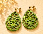 Paire de boucles d'oreilles en résine acrylique verte marbrée en forme de goutte sculptée, montées sur tiges dorées, fond bois avec fleurs séchées