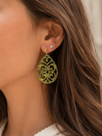 Boucles d'oreilles pendantes en acrylique vert marbré découpé à motif arabesque, avec attache dorée ovale, portées par une femme aux cheveux bruns