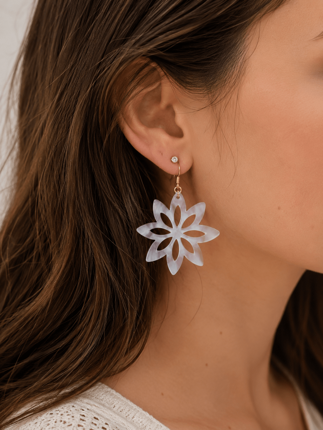 Boucles d'oreilles pendantes en acrylique blanc nacré en forme de fleur étoilée ajourée, montées sur crochet doré, portées par une femme aux cheveux bruns