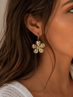 Boucles d'oreilles créoles dorées avec charm fleur martelée à 6 pétales ronds, portées par une femme aux cheveux ondulés
