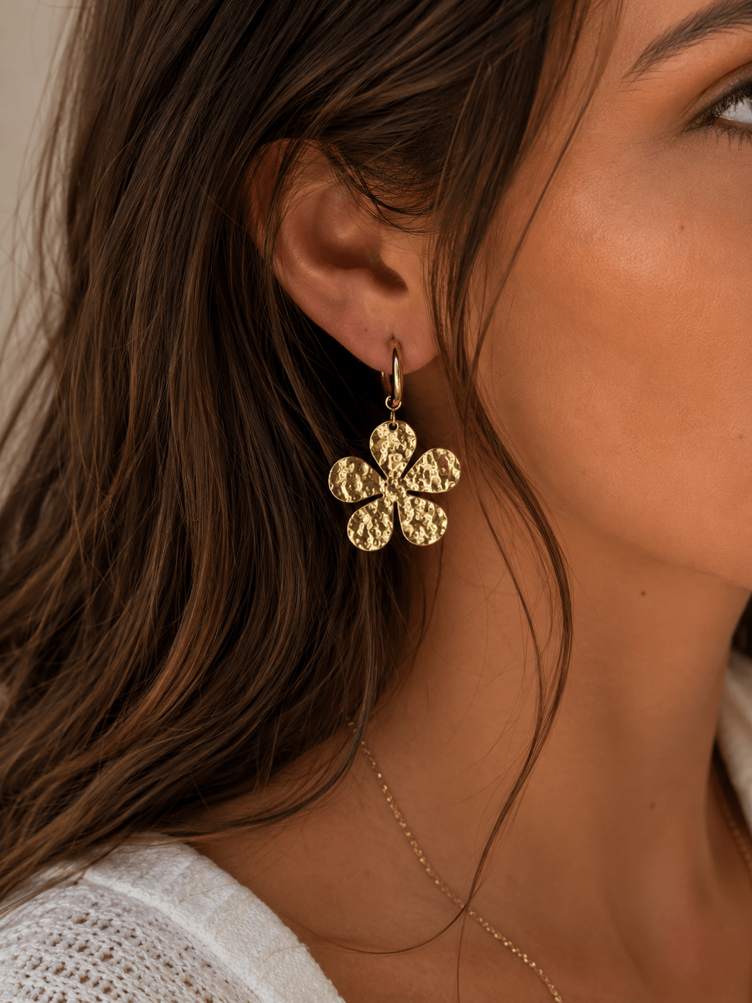 Boucles d'oreilles créoles dorées avec charm fleur martelée à 6 pétales ronds, portées par une femme aux cheveux ondulés