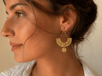 Boucles d'oreilles dorées martelées en forme de croissant, suspendues par une chaîne fine à une puce boule dorée, portées par une femme aux cheveux relevés