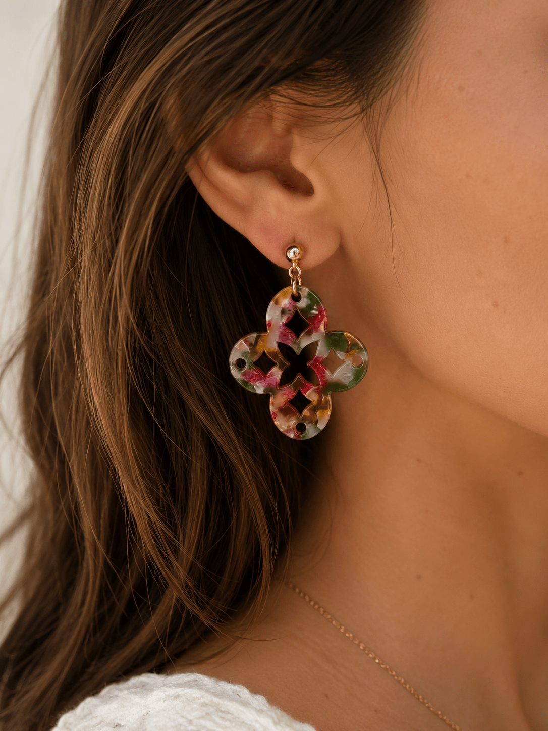 Boucles d'oreilles pendantes en acrylique multicolore (rose, vert, orange) en forme de trèfle ajouré, montées sur puce boule dorée, portées par une femme
