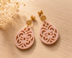 Paire de boucles d'oreilles en acrylique rose nude en forme de goutte ajourée motif baroque, montées sur puces dorées texturées, fond bois clair