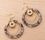 Paire de boucles d'oreilles pendantes composées d'un grand cercle acrylique effet zébré noir et blanc, d'un anneau doré martelé et d'un médaillon étoile dorée, crochets dorés