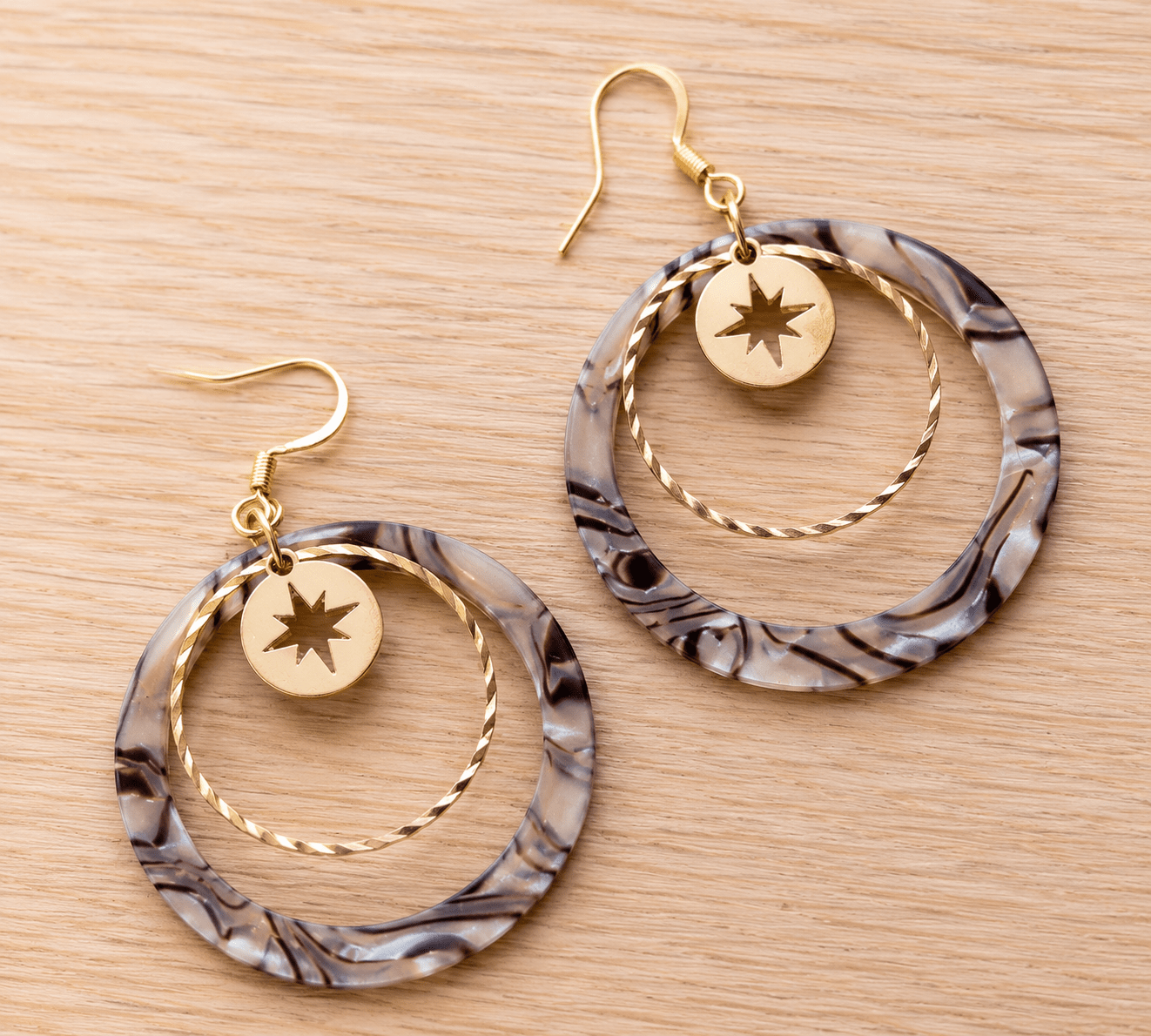 Paire de boucles d'oreilles pendantes composées d'un grand cercle acrylique effet zébré noir et blanc, d'un anneau doré martelé et d'un médaillon étoile dorée, crochets dorés