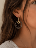 Boucles d'oreilles créoles zébrées noir et blanc avec anneau doré et médaillon étoile polaire, portées par une femme aux cheveux bruns ondulés