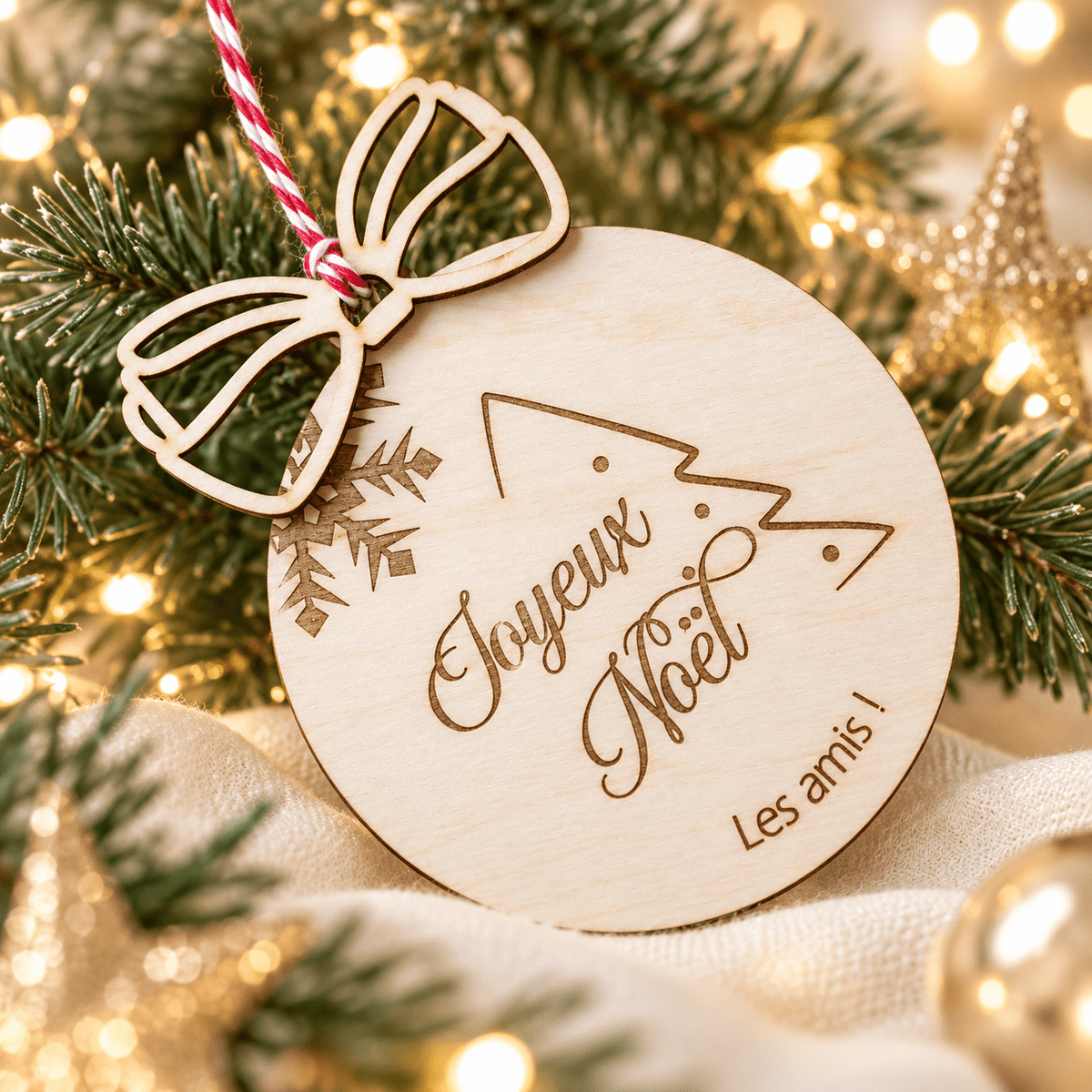 Boule de Noël en bois modèle sapin gravée « Joyeux Noël » et « Les amis ! », suspendue dans un sapin illuminé