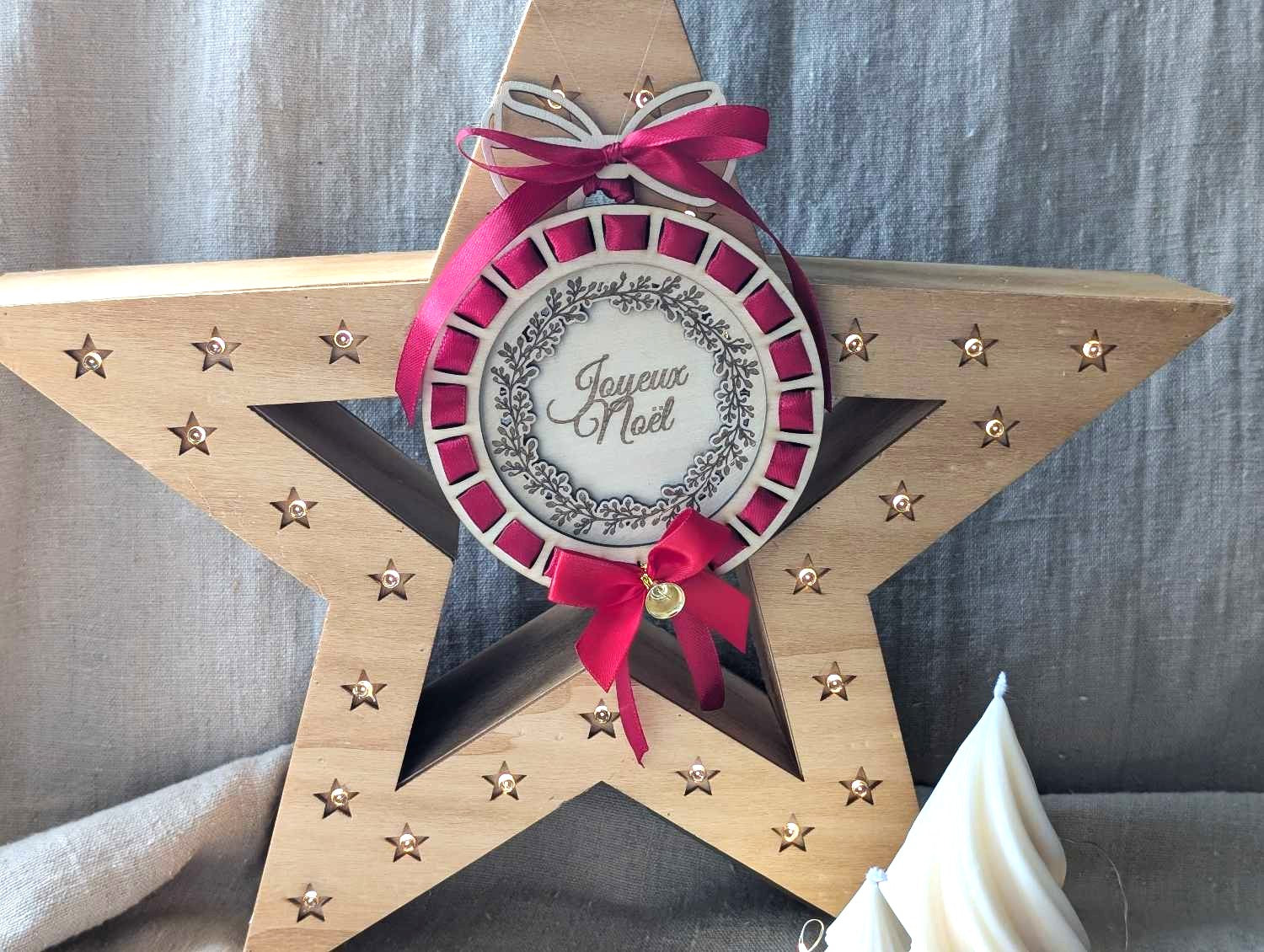 Boule de Noël personnalisée en bois naturel gravé avec ruban rouge profond entrelacé effet cocarde, texte Joyeux Noël et couronne de feuillage gravée au laser