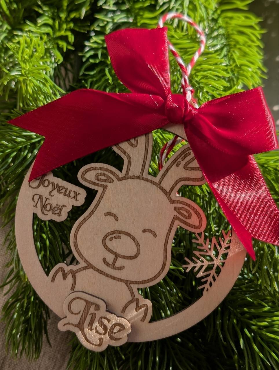 Boule de Noël en bois avec renne et flocon gravés, prénom personnalisé et gros nœud rouge, collection Artesama