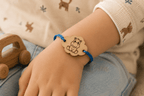 Bracelet enfant en bois gravé motif hippopotame rigolo sur cordon bleu ajustable, porté au poignet d'un enfant, avec jouets en bois en arrière-plan
