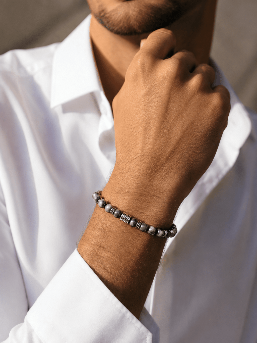 Bracelet homme perles de labradorite gris-noir avec perle centrale argentée gravée motif méandre, porté au poignet d'un homme en chemise blanche