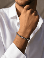 Bracelet homme perles de labradorite gris-noir avec perle centrale argentée gravée motif méandre, porté au poignet d'un homme en chemise blanche