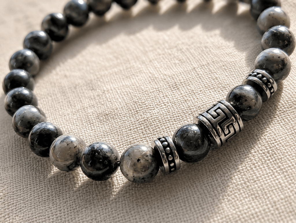 Gros plan sur bracelet homme perles de labradorite gris marbré avec perle centrale et rondelles argentées gravées motif méandre grec, sur fond lin naturel