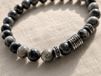 Gros plan sur bracelet homme perles de labradorite gris marbré avec perle centrale et rondelles argentées gravées motif méandre grec, sur fond lin naturel