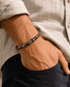 Bracelet homme perles de labradorite naturelles avec accent argenté gravé, porté au poignet d'un homme en chemise lin beige, main dans la poche