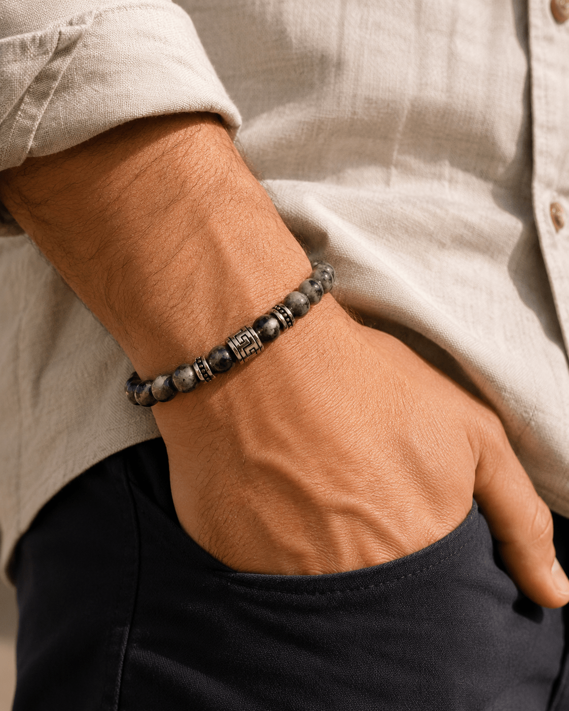 Bracelet homme perles de labradorite naturelles avec accent argenté gravé, porté au poignet d'un homme en chemise lin beige, main dans la poche