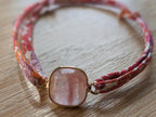 Gros plan pierre rose naturelle sertie dans monture dorée sur bracelet ruban Liberty fleuri rose