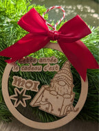 Boule de Noël artisanale en bois, bébé gnome qui sort d'un cadeau et message “Cette année le cadeau c’est moi”