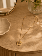 Collier médaillon étoile doré posé sur meuble en bois ambiance lumineuse dorée, bijou artisanal acier