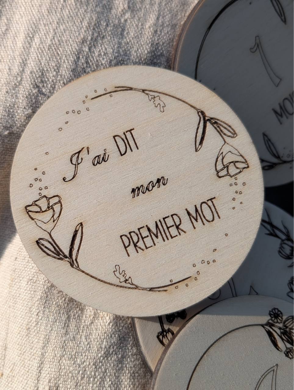 Détail d’une carte étape bébé en bois gravée au prénom, finition naturelle. "j'ai dit mon premier mot".