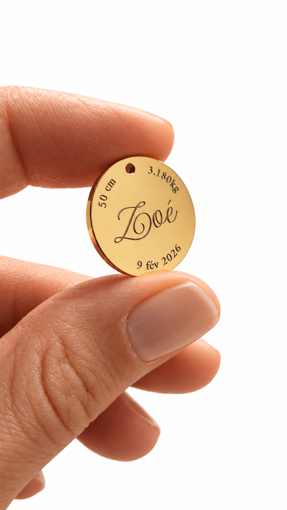 Médaillon de naissance doré gravé du prénom Zoé, de la date de naissance, du poids et de la taille, tenu entre deux doigts