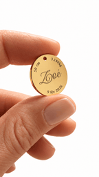 Médaillon de naissance doré gravé du prénom Zoé, de la date de naissance, du poids et de la taille, tenu entre deux doigts