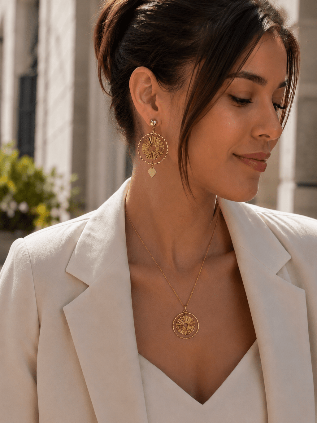 Femme portant une parure soleil dorée boucles pendantes cercle rayonnant et collier médaillon acier doré