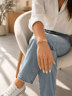 Bracelet liberty fleuri rose et vert avec fermoir toggle doré, porté au poignet d'une femme en jean et chemise blanche dans un intérieur lumineux