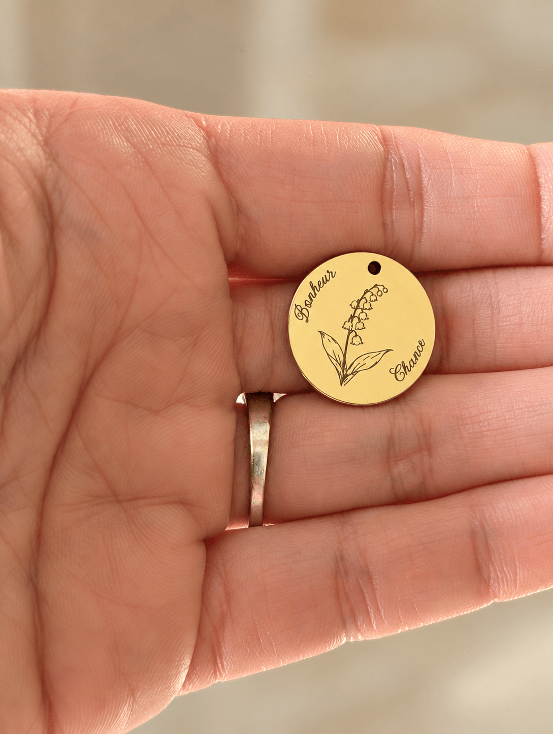 Médaillon gravé du muguet, fleur de naissance de mai, avec les mots Bonheur et Chance, posé dans la paume d'une main