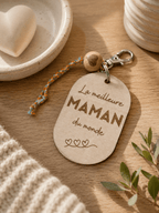 Porte-clés en bois gravé Meilleure Maman du Monde posé sur une table en bois, détail perle et mousqueton argenté