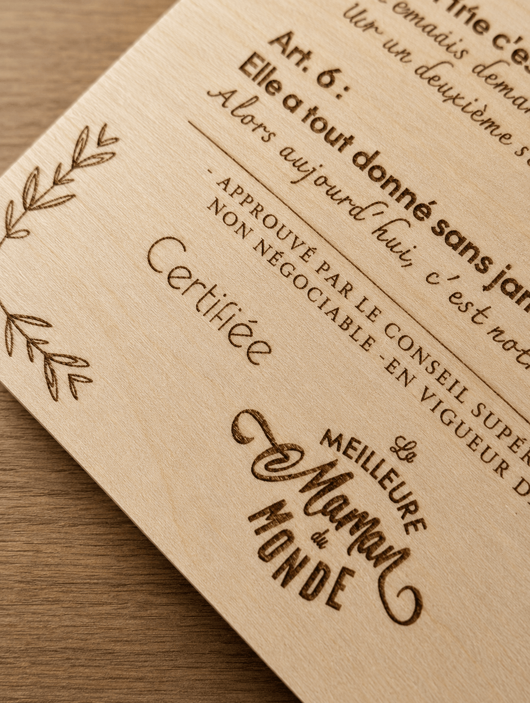 Gros plan de la gravure laser sur plaque bois clair, mention Certifiée La Meilleure Maman du Monde gravée avec précision